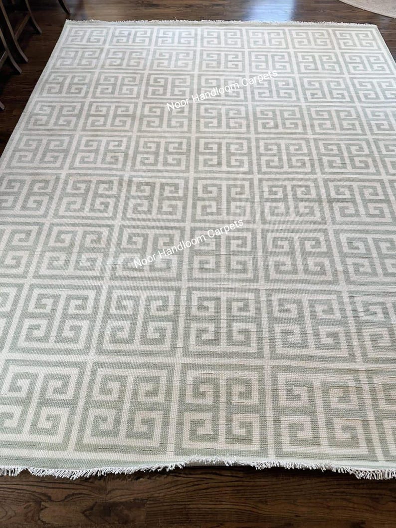 May include: A rectangular rug with a repeating geometric pattern in light gray and white. The rug has a fringed edge and the text "Noor Handsome Carpets" is visible on the rug.