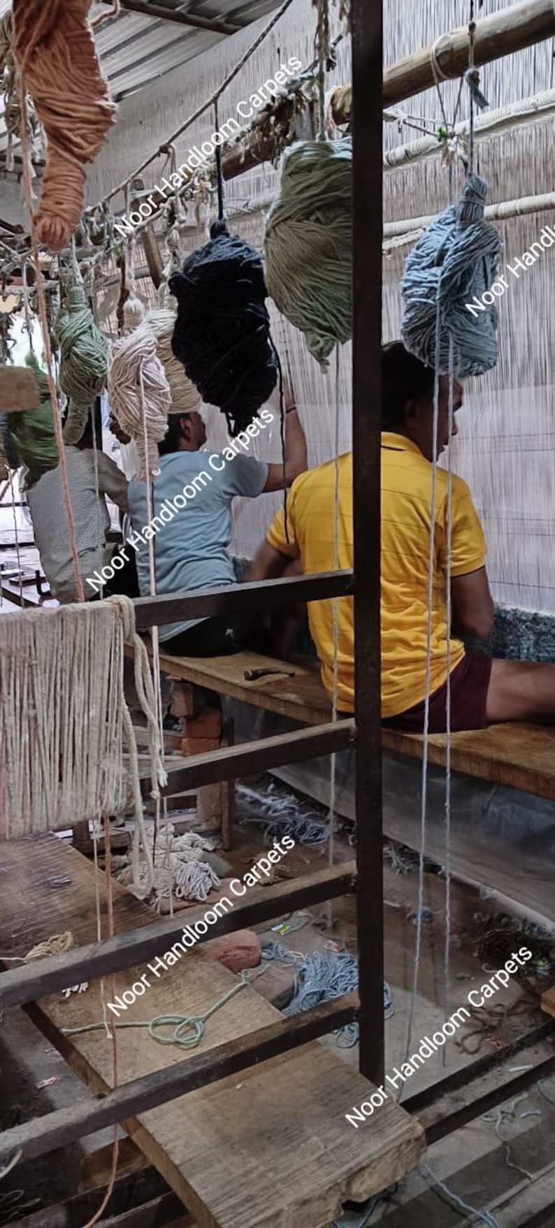 May include: Artisans weaving a carpet on a wooden loom. Various colored yarn bundles hang above the loom. The image shows the process of creating a handmade carpet. The text "Noor Handloom Carpets" is visible.