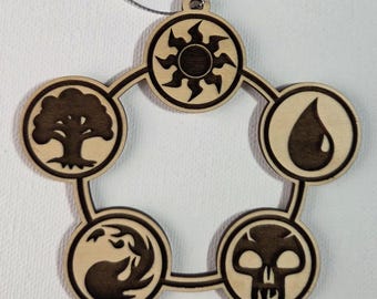 May include: Wooden ornament featuring a circular design with five interconnected circles, each displaying a different symbol. The symbols include a sun, a tree, a water droplet, a skull, and a swirling design. A silver string is attached for hanging.