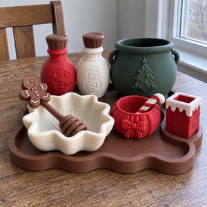 May include: A brown scalloped tray holding a collection of holiday-themed items: a red bottle with a snowflake, a white bottle with a snowman, a green cauldron with a tree, a white bowl with a gingerbread man stirrer, a red bowl, and a chimney.