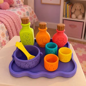 Pode incluir: Um conjunto de brinquedos de silicone coloridos para fazer poções numa bandeja roxa, incluindo três garrafas com rolhas castanhas, um caldeirão roxo com uma colher amarela e três copos pequenos com desenhos de estrela, gota e flor.