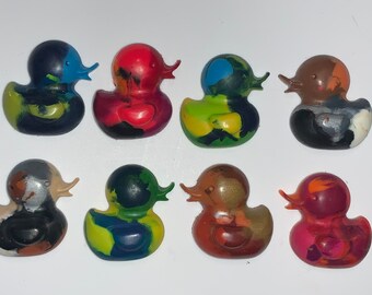 May include: Eight colorful rubber duck toys made of crayon wax. The ducks are in various colors, including red, blue, green, yellow, orange, brown, black, and silver.