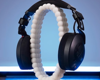 May include: Black over-ear headphones with a white, beaded stand. The headphones have a black headband and earcups with a silver accent.