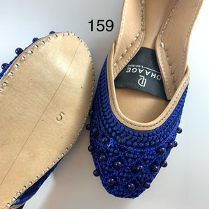 May include: A pair of blue velvet shoes with beaded embellishments. The shoes have a pointed toe and a low heel. The brand name "DHAGE London" is visible on the inside of the shoe.