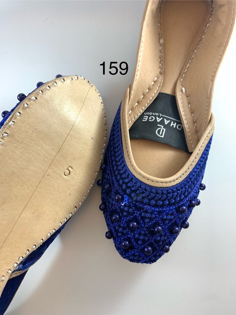 May include: A pair of blue velvet shoes with beaded embellishments. The shoes have a pointed toe and a low heel. The brand name "DHAGE London" is visible on the inside of the shoe.