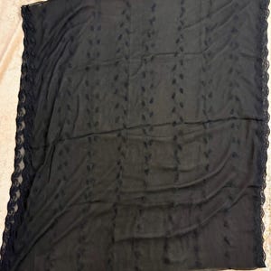 May include: A rectangular black scarf made of a sheer, lightweight fabric. The scarf features vertical rows of small, embroidered leaf-like patterns throughout the center and is finished with a decorative scalloped lace trim along both side edges.
