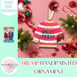 May include: Hand-painted Christmas ornament shaped like a red and white sweater with the text "Maga Bullet Proof" in gold lettering. The ornament is surrounded by red and gold Christmas ornaments.