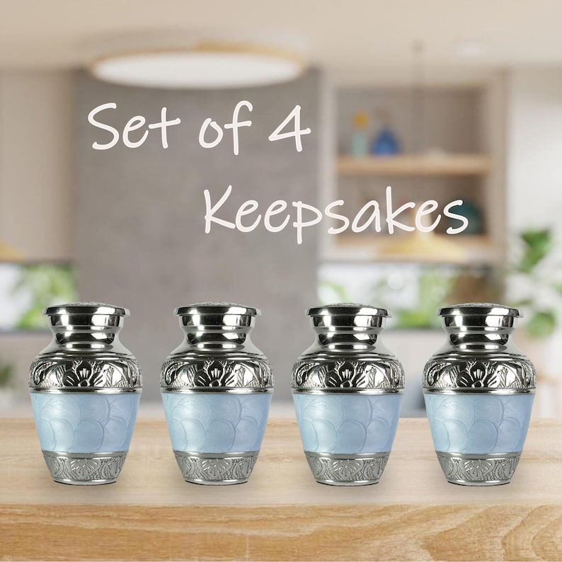 May include: Set of four keepsake urns. Each urn features a light blue base with a floral design, silver-colored accents, and a matching lid. The urns are displayed on a wooden surface.