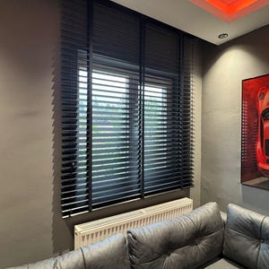 May include: Black horizontal window blinds installed over a rectangular window. The blinds feature thin, adjustable slats that allow light to filter through, covering the glass pane entirely while mounted within the window frame structure.