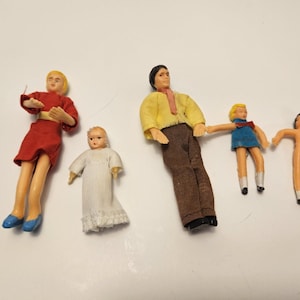 May include: A collection of vintage dollhouse dolls. The dolls include a woman in a red dress, a baby in a white dress, a man in a yellow shirt and brown pants, and two children. The dolls are made of plastic.
