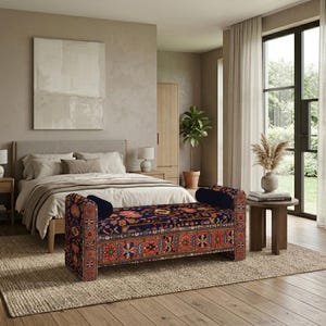 Puede incluir: Un banco rectangular tapizado con una base azul oscuro y complejos patrones florales y geométricos en rojo, naranja y crema. El banco cuenta con dos cojines cilíndricos de color azul oscuro a juego situados en cada extremo del asiento.