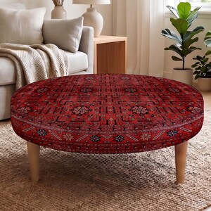 Puede incluir: Un taburete redondo con tapicería de tela roja intensa y un detallado patrón geométrico en blanco y negro. La pieza se apoya sobre cuatro patas de madera clara que se estrechan hacia el suelo, proporcionando una base estable al asiento.