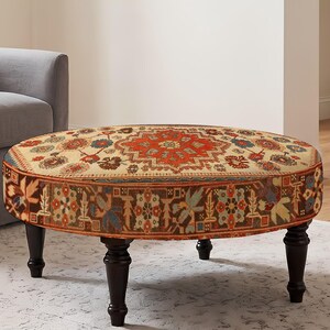 Könnte beinhalten: Ein runder Hocker mit cremefarbener Oberseite und einem zentralen geometrischen Medaillonmuster in Rot und Blau. Die Seiten sind mit dunkelbraunem Stoff mit mehrfarbigem Blumenmuster bezogen und stehen auf vier dunkelbraunen gedrechselten Holzbeinen.