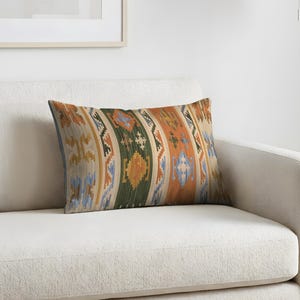 May include: A rectangular throw pillow featuring a woven pattern of vertical stripes in shades of forest green, burnt orange, light blue, and cream. The design includes repeating geometric shapes and cross motifs across the entire surface.