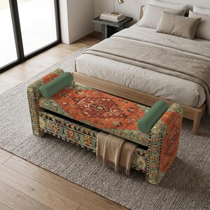 May include: A rectangular storage bench upholstered in a vibrant orange and teal patterned fabric with a traditional motif. The bench features two solid sage green cylindrical bolster pillows at each end and a beige throw blanket draped over the front.