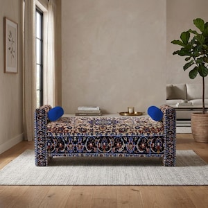 May include: A rectangular bench featuring a detailed floral and geometric pattern in shades of blue, red, and cream. The bench has two upright armrests, each accented with a solid bright blue cylindrical bolster pillow at the top inner edge.