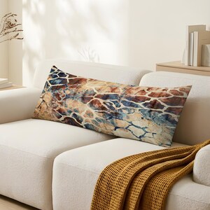 Könnte beinhalten: Ein rechteckiges Dekokissen mit einem lebendigen, mehrfarbigen abstrakten Muster, das an eine rissige oder marmorierte Oberfläche erinnert. Das Design kombiniert tiefe Blau-, warme Braun-, Beige- und Cremetöne und erzeugt ein komplexes, ineinandergreifendes Netzwerk aus Formen auf der gesamten Oberfläche des Kissenbezugs.