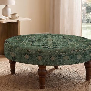 May include: A round ottoman featuring a dark green fabric upholstery with a detailed, symmetrical floral and geometric pattern. The piece is supported by four turned, dark brown wooden legs that provide a stable base for the circular seat.