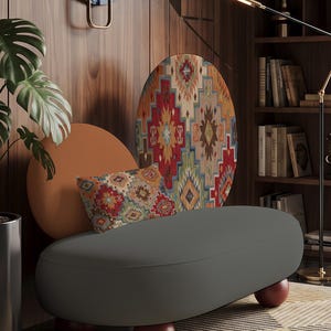 May include: A gray oval-shaped bench with rounded dark red feet. Behind the bench is a large circular panel featuring a colorful geometric pattern in red, orange, blue, and green, alongside a smaller solid orange circle and a rectangular pillow.