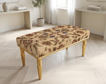 May include: A rectangular bench featuring a beige upholstered seat with a multi-colored floral and paisley pattern. The bench is supported by four tapered, gold-finished legs with a smooth, polished surface and a rounded, turned design.