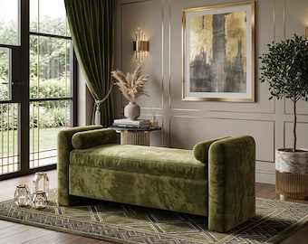 May include: An olive green velvet storage bench featuring a rectangular seat, two cylindrical bolster pillows at each end, and a smooth upholstered finish. The bench is positioned on a patterned rug with geometric lines in shades of green and gray.