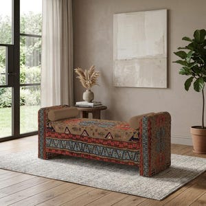 Puede incluir: Un banco rectangular con tapicería textil estampada con motivos geométricos en tonos bronceado, rojo y azul. El banco incluye dos cojines cilíndricos de color bronceado sólido, colocados en cada extremo del asiento.