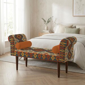 Può includere: Una panca da camera da letto caratterizzata da un motivo geometrico multicolore nei toni dell'arancione, del blu e della crema. La panca presenta due braccioli curvi, quattro gambe in legno marrone scuro e due cuscini cilindrici arancioni.
