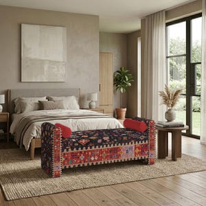 May include: A rectangular upholstered bench featuring a dark fabric with a multi-colored geometric pattern and a wide red border. The bench includes two cylindrical red bolster pillows at each end and stands on short, sturdy wooden legs.