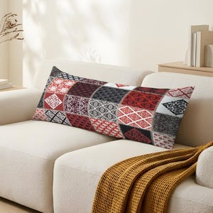 Puede incluir: Un cojín lumbar rectangular con un diseño de patchwork compuesto por varios cuadrados de tela. Los patrones incluyen motivos florales, damascos y geométricos en rojo, negro, blanco y gris. Los cuadrados están unidos por costuras visibles en cuadrícula.
