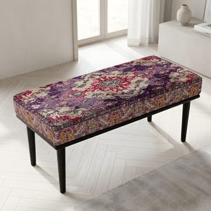 May include: A rectangular bench featuring a cushioned seat upholstered in a vibrant fabric with a complex, multi-colored floral and geometric pattern in shades of deep purple, magenta, cream, and gold, supported by four tapered black wooden legs.