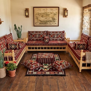 May include: A set of three light-colored wooden sofas with red, black, and white patterned cushions and matching bolsters. The arrangement includes a central floor cushion and a rectangular rug featuring the same geometric textile design.