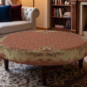 May include: A round ottoman featuring a terracotta-coloured top with a floral pattern and a cream-coloured side panel decorated with a lattice design and floral motifs. The piece is supported by four dark brown wooden legs with a turned design.