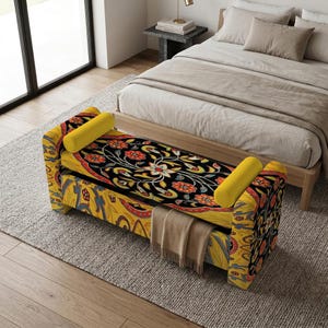 Puede incluir: Un banco tapizado rectangular con una parte superior negra con un vibrante estampado floral en rojo, naranja y blanco. Los lados y la base muestran un fondo amarillo con intrincados diseños azules y rojos, complementados por dos cojines cilíndricos amarillos.