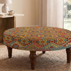 Puede incluir: Un taburete redondo con un vibrante patrón geométrico multicolor en tonos rojo, amarillo, azul y verde. La pieza se apoya sobre cuatro patas de madera torneada de color marrón oscuro que proporcionan una base estable al asiento circular.