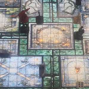 May include: A tabletop role-playing game board with various illustrated tiles depicting rooms and corridors. Miniature figures and dice are scattered across the board. The tiles are primarily shades of gray, blue, and green.