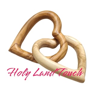 May include: Two interlocking wooden hearts, carved from olive wood, in a light brown color. The hearts are intertwined, creating a symbol of love and unity.