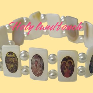 May include: White bracelet with pearl accents and rectangular charms featuring religious images. The bracelet has the text "Holy Land Touch" on it.
