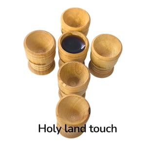 Pode incluir: Copos de madeira castanho-claro dispostos em forma de cruz, um deles cheio de um líquido escuro. Os copos têm uma base arredondada e a palavra "Jerusalem" está impressa na lateral. O texto "Holy land touch" está na parte inferior.
