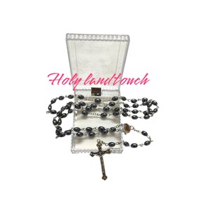 May include: A black rosary with a silver cross and beads in a clear plastic box. The box has the text "Holy land touch" printed on it.