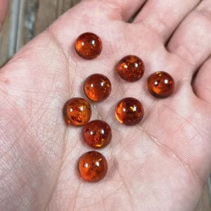May include: Eight amber glass marbles with a golden shimmer. The marbles are round and smooth, and they are arranged in a loose pile on a hand.