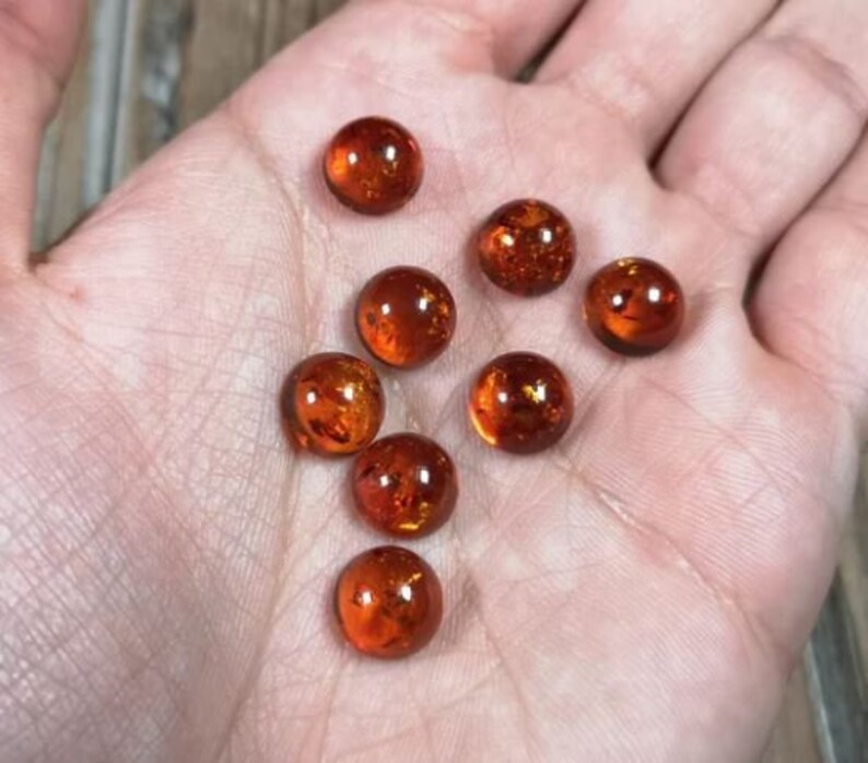 May include: Eight amber glass marbles with a golden shimmer. The marbles are round and smooth, and they are arranged in a loose pile on a hand.