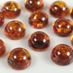 May include: A collection of round, amber-colored cabochons. The cabochons are smooth and have a glossy finish. They are arranged in a random pattern on a white surface.