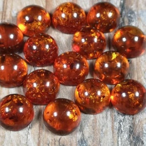 May include: A collection of 14 round, amber cabochons. The cabochons are smooth and polished, with a warm, honey-like color. They are all approximately the same size and shape.
