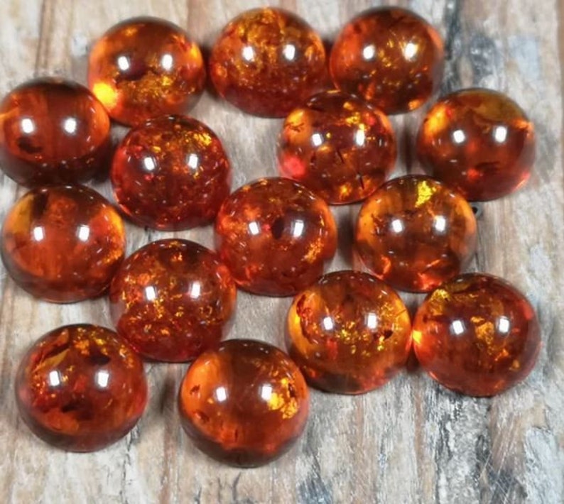 May include: A collection of 14 round, amber cabochons. The cabochons are smooth and polished, with a warm, honey-like color. They are all approximately the same size and shape.