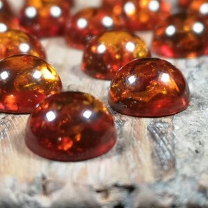 May include: A collection of round, amber-colored cabochons, with a smooth, polished surface. The cabochons are arranged in a random pattern on a wooden surface.