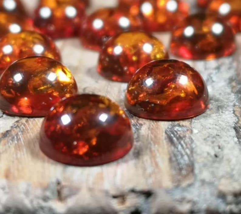 May include: A collection of round, amber-colored cabochons, with a smooth, polished surface. The cabochons are arranged in a random pattern on a wooden surface.