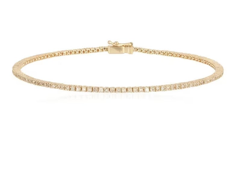 Puede incluir: Un brazalete de tenis de oro con una fila de peque&ntilde;os diamantes transparentes.