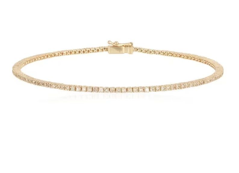 Puede incluir: Un brazalete de tenis de oro con una fila de peque&ntilde;os diamantes transparentes.