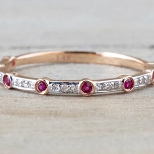 以下が含まれることがあります： 小さなダイヤモンドと5つのルビーの宝石が並んだ、繊細なローズゴールドのバンドリングです。