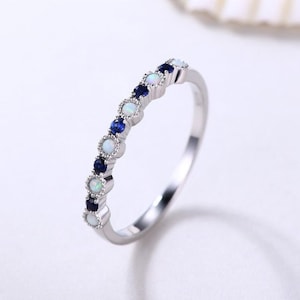 May include: A silver band ring with alternating white opal and blue sapphire stones.